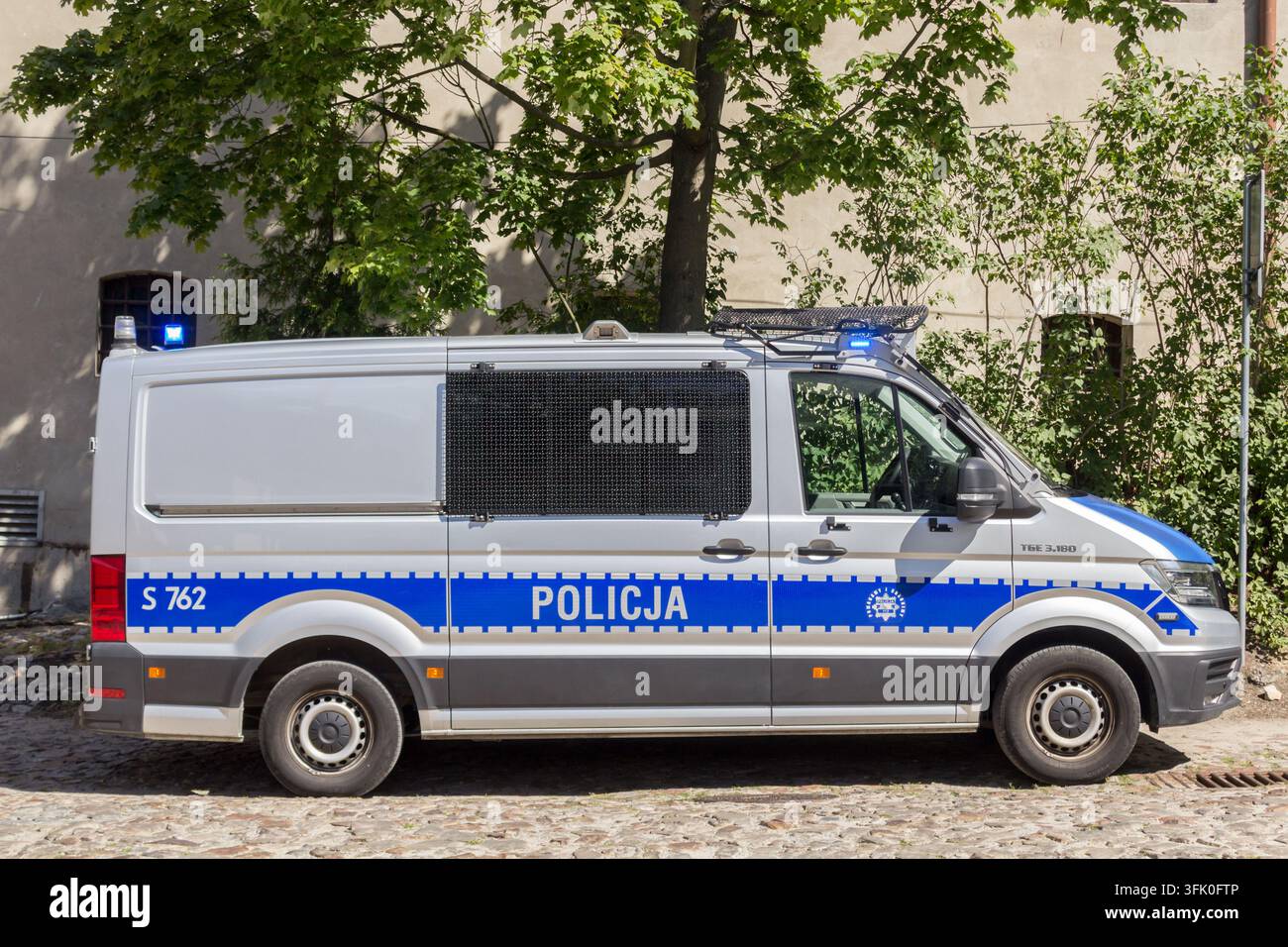 Furgone della polizia polacca parcheggiato accanto a un edificio, con luci di emergenza blu e marchi ufficiali POLICJA. Foto Stock
