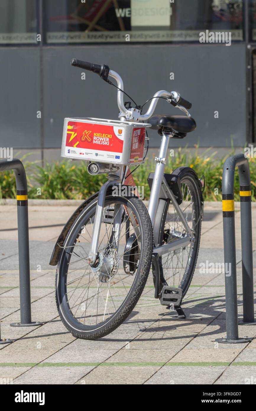 Bicicletta urbana parcheggiata a un rastrelliera pubblica accanto a un edificio urbano, con un pannello di informazioni sulla noleggio rosso attaccato. Foto Stock