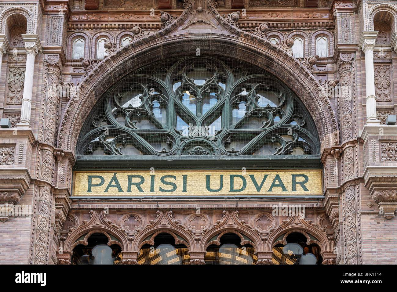 Un rosone metallico verde con traforo floreale corona l'insegna dorata Parisi Udvar sopra una fila di porte ad arco, la cui muratura circostante è scolpita w Foto Stock