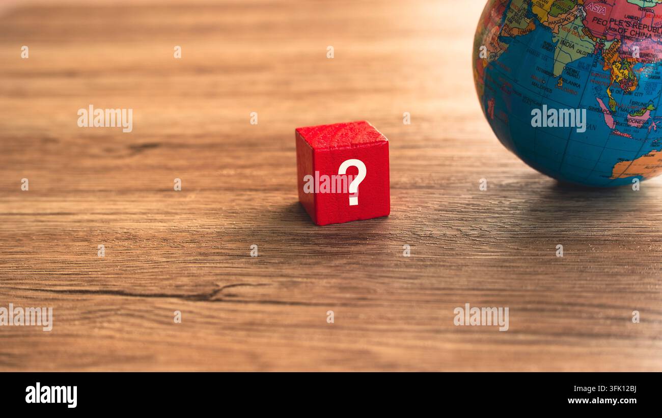 Blocco punto interrogativo rosso accanto a un globo terrestre su sfondo di legno – concetto di incertezza globale per il business internazionale Foto Stock
