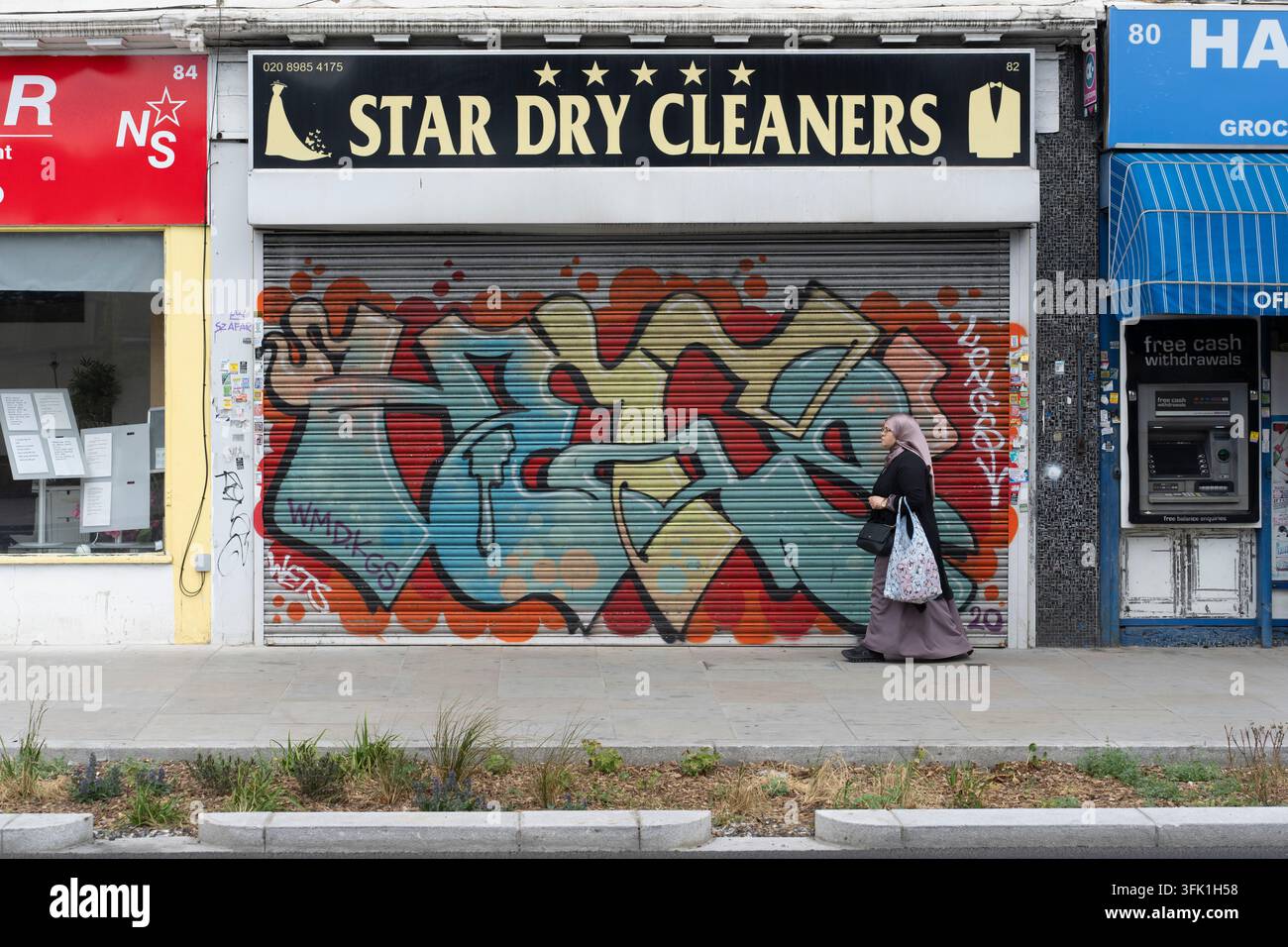 Una donna passa davanti a Star Dry Cleaners al 82 Amhurst Road, Hackney Central, Londra, passando davanti alle saracinesche coperte di graffiti del negozio. Foto Stock