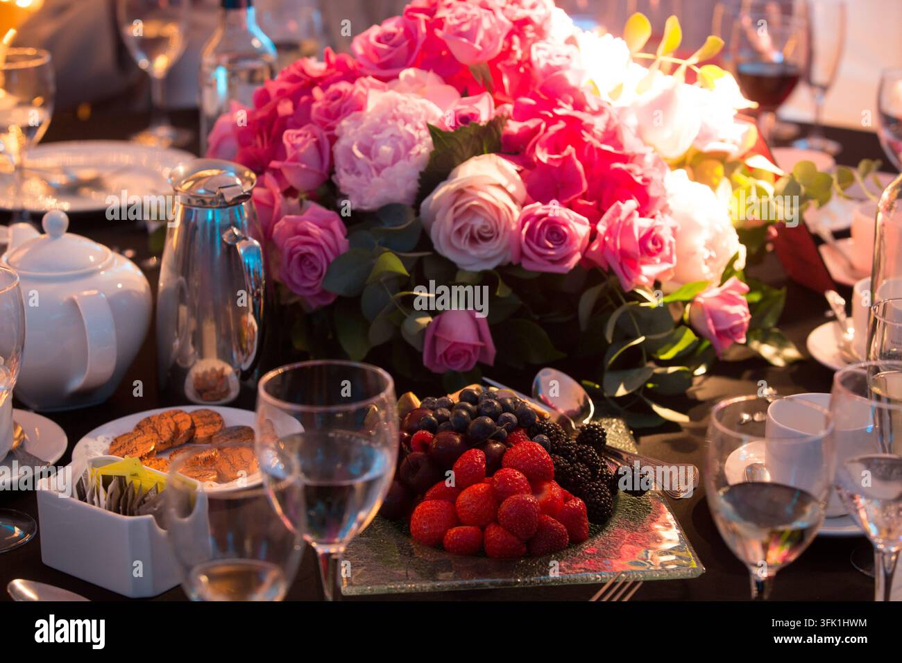 Gli ospiti celebrano un evento speciale a un tavolo da banchetto di lusso adornato con rose rosa e bacche fresche. Foto Stock