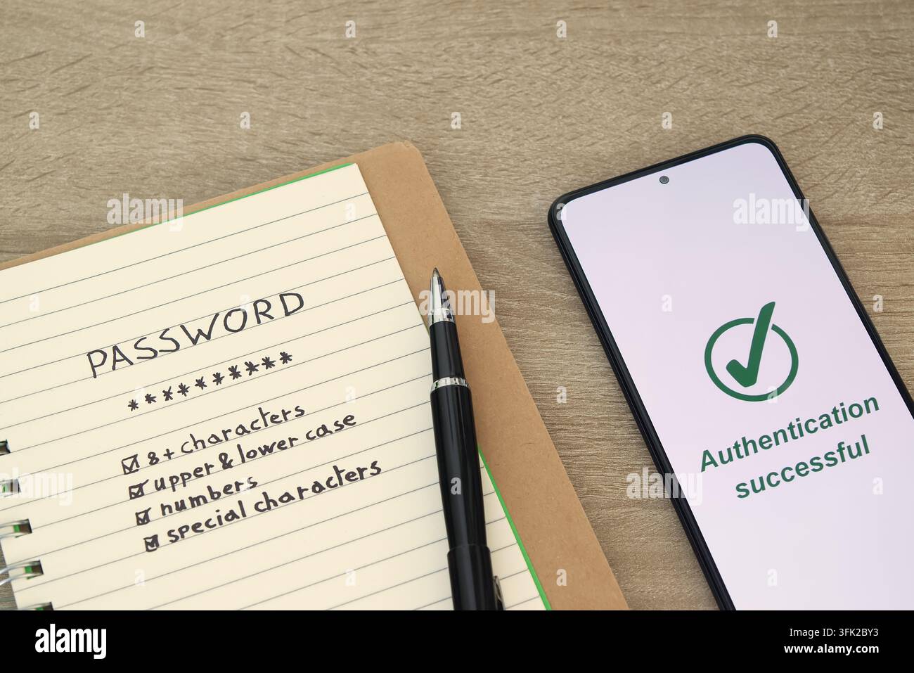 Vista ravvicinata dettagliata di consigli di sicurezza per le password scritti a mano in un taccuino accanto a uno smartphone che conferma l'autenticazione riuscita con un segno di spunta verde Foto Stock