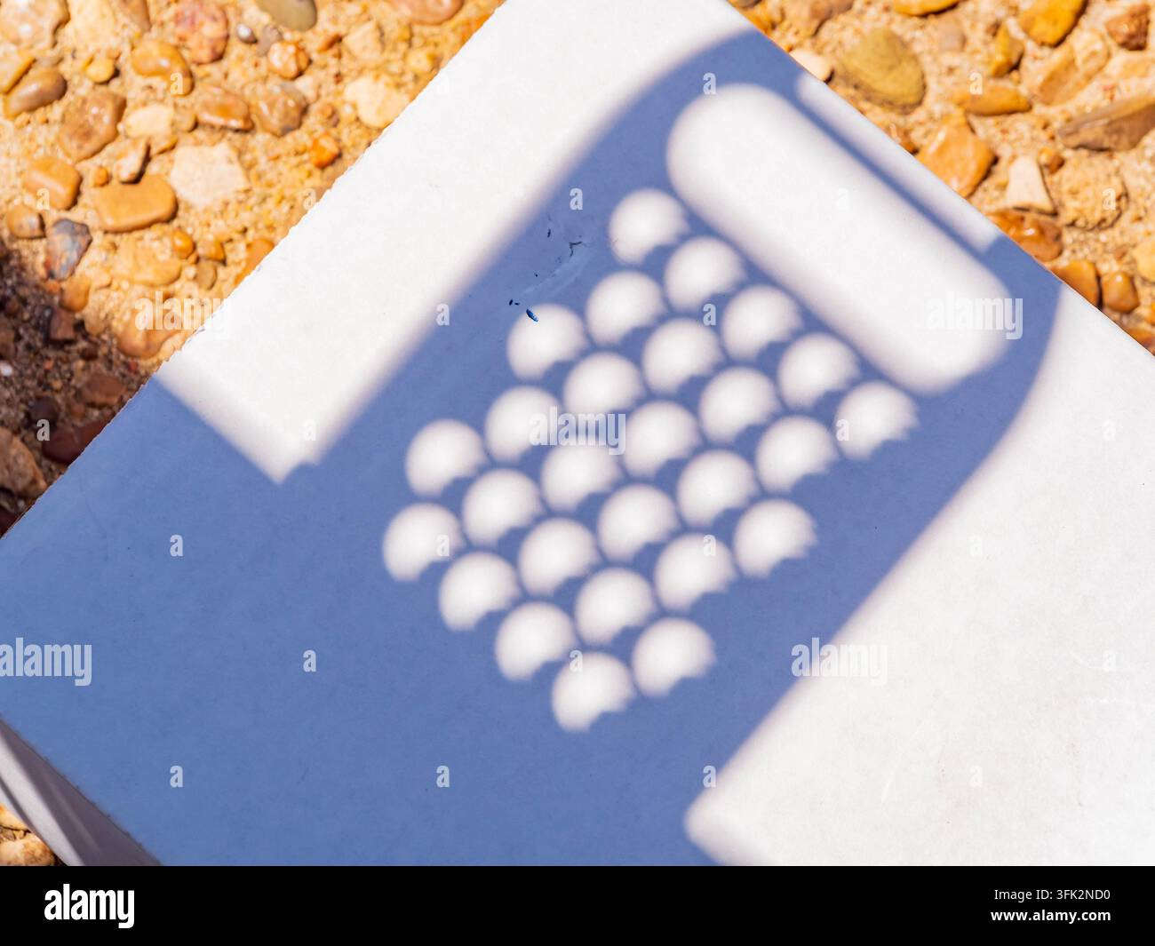 Un'ombra geometrica con motivi circolari si estende su uno sfondo bianco pulito appoggiato su un letto di piccoli ciottoli. Foto Stock