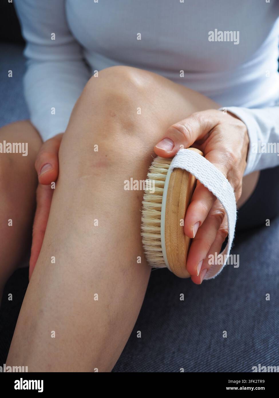 Donna matura che usa una spazzola di legno per il corpo sul ginocchio e sulla gamba a casa per la cura di sé Foto Stock