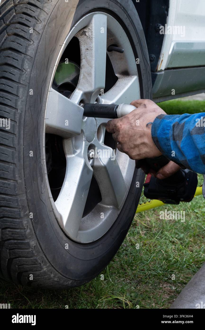 Meccanico che usa una chiave a impatto per cambiare una ruota dell'auto, primo piano Foto Stock