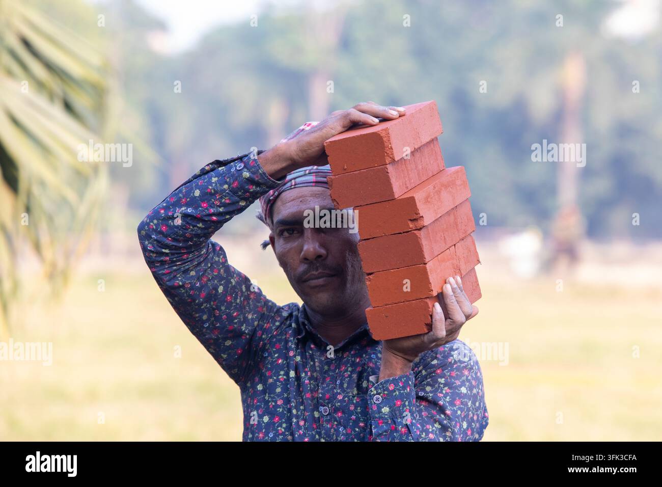 Un operaio edile porta diverse mattonelle tra le mani in un cantiere a Dhaka, Bangladesh. Foto Stock