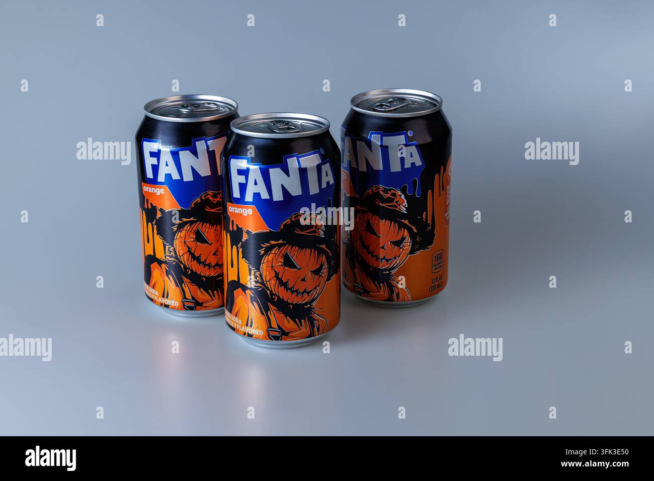 Tre lattine di soda arancione Fanta con illustrazioni di zucca e strega di Halloween disposte su uno sfondo blu, concetto di bevanda stagionale festiva. Foto Stock