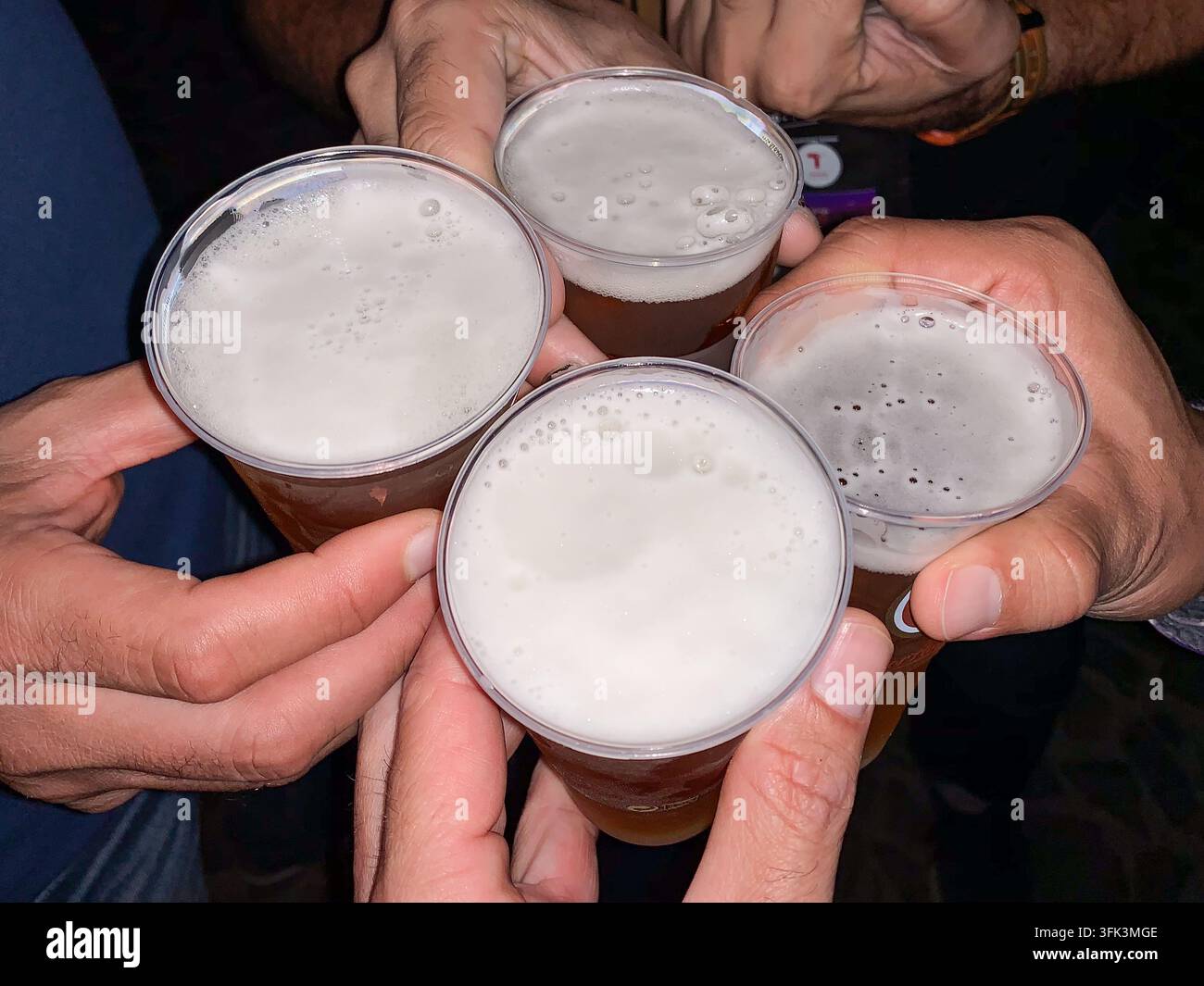 Quattro mani avvicinano bicchieri di birra per un brindisi celebrativo durante una visita a Lisbona, Portogallo. Foto Stock