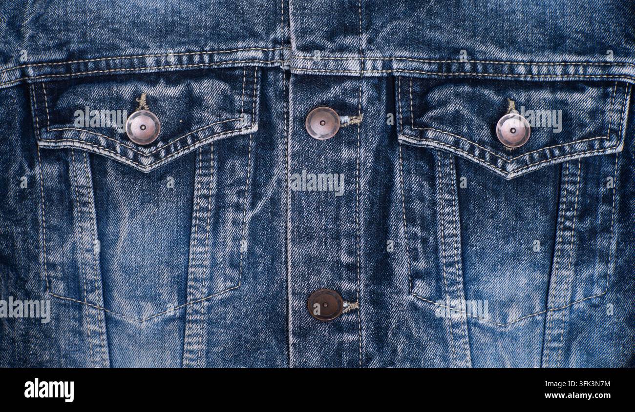 Parte superiore di giacca in denim blu con tasche a patella, bottoni in metallo, cuciture verticali e texture tessile sbiadita. Foto Stock