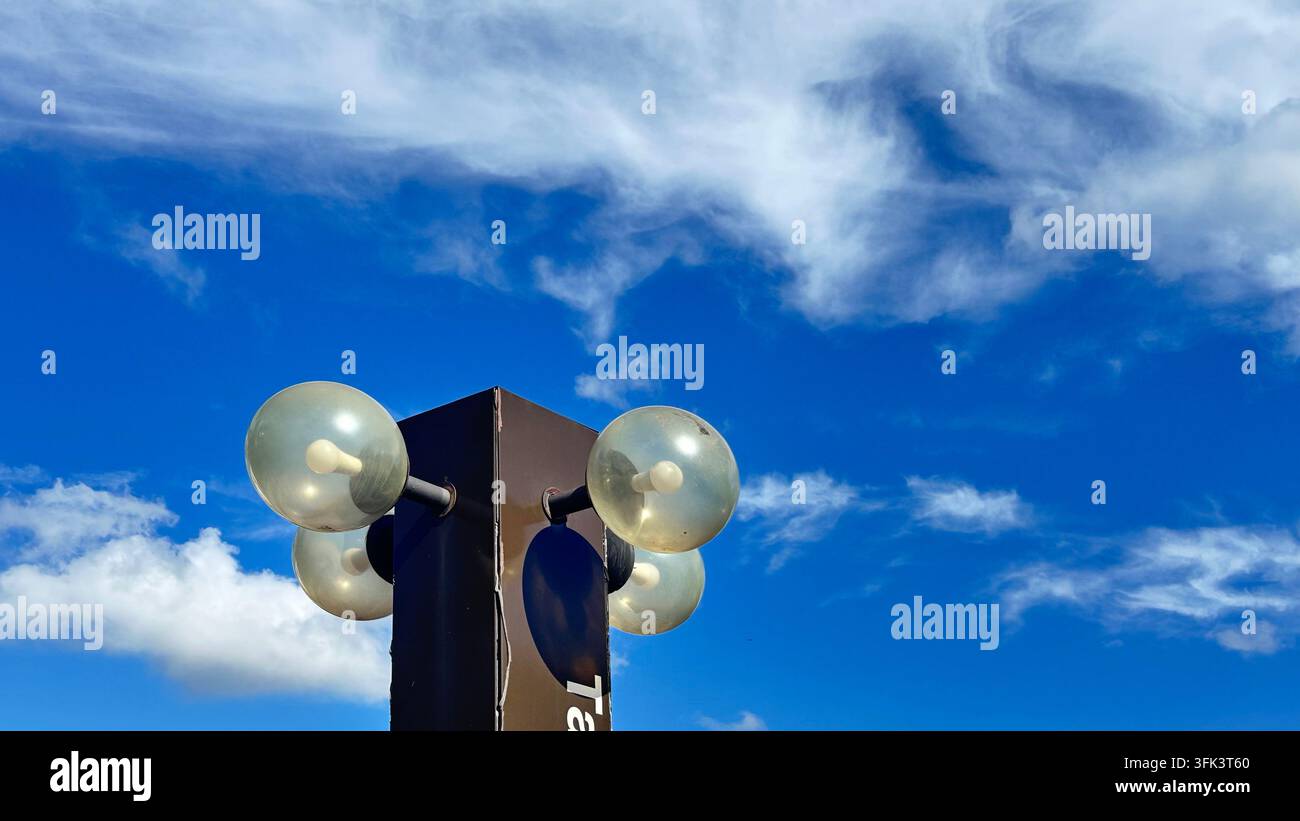 Una lampada da esterno marrone scuro a più globi o supporto su un cielo blu brillante con nuvole sottili. Foto Stock