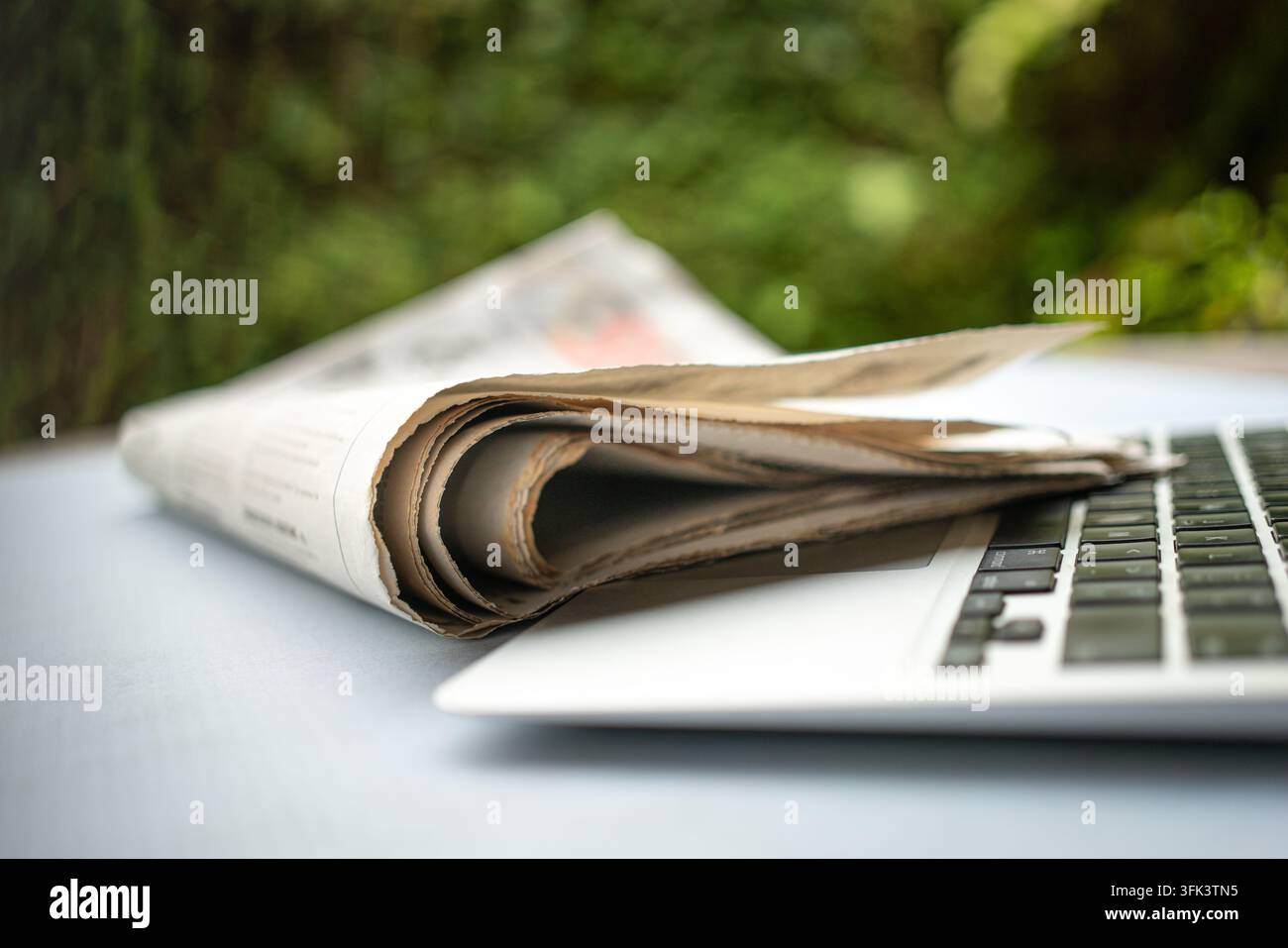 Giornale sopra un computer portatile, sfondo di giardino verde. Concetto di media tradizionali versus digitali. Foto Stock