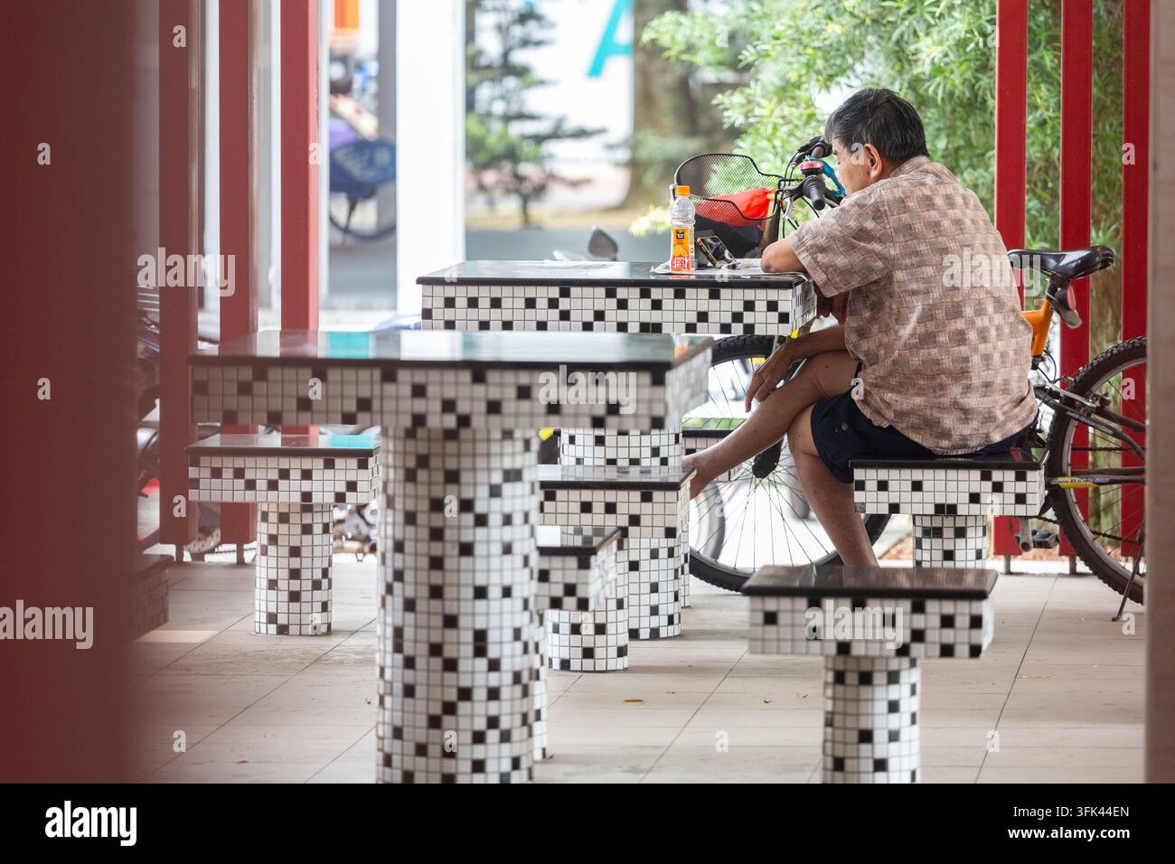 Negli spazi pubblici dei Void Decks, un anziano in pensione guarda uno spettacolo sull'app del suo telefono cellulare per passare il tempo, Singapore. Foto Stock