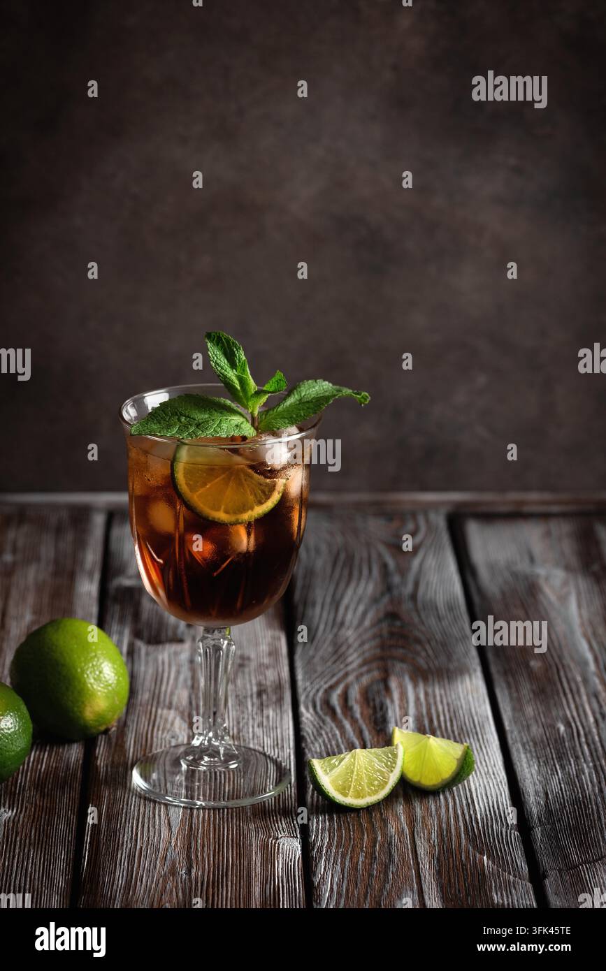 Cuba Libre in un bicchiere con rum marrone, cola-lime, menta su uno sfondo di legno scuro. Vista laterale, messa a fuoco selettiva. Foto Stock