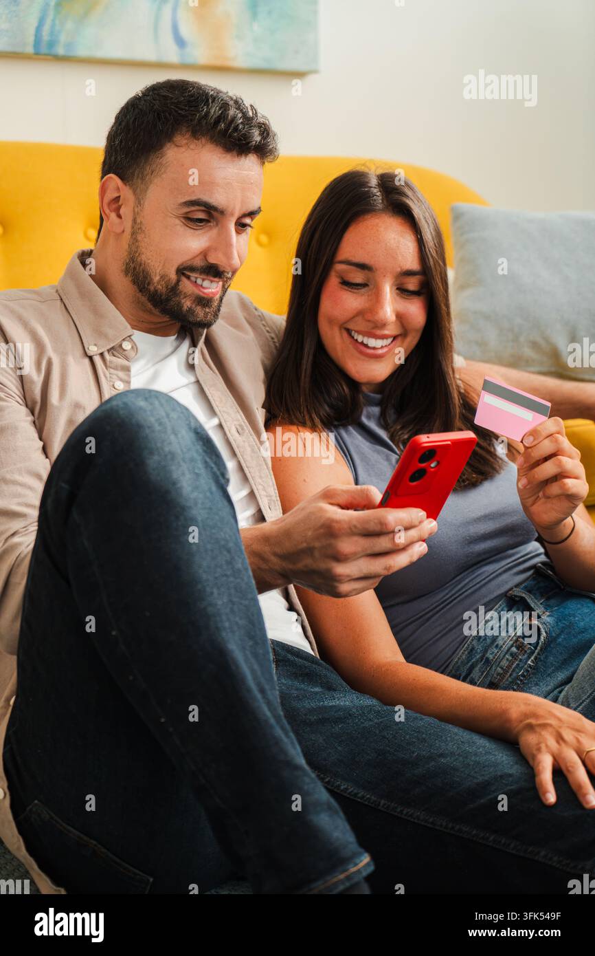 Una coppia sorridente si siede insieme con un telefono e una carta, sfoglia offerte online e prende una decisione condivisa sugli acquisti in un momento confortevole a casa Foto Stock