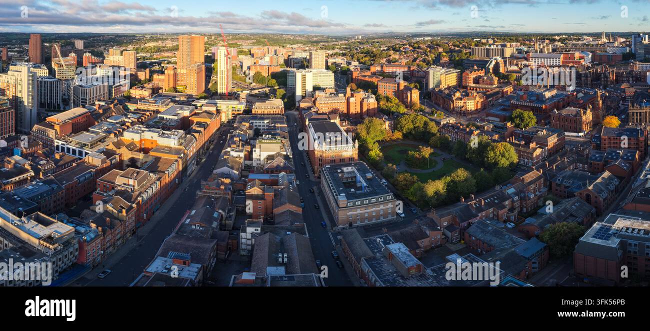 Panorama aereo che si affaccia sul nucleo urbano di Leeds, i quartieri storici in mattoni rossi, un parco cittadino quadrato verde e la lontana skyline immersa nella luce del mattino. Foto Stock