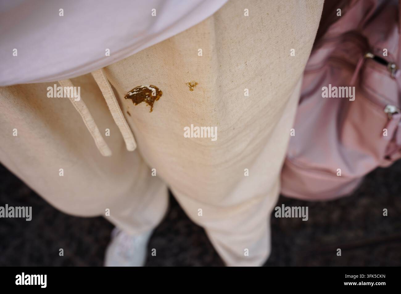 Macchia evidente di escrementi di uccello su pantaloni casual beige, che illustra vestiti sporchi, disordine all'aperto inaspettato e il concetto di rimozione delle macchie sul tessuto Foto Stock