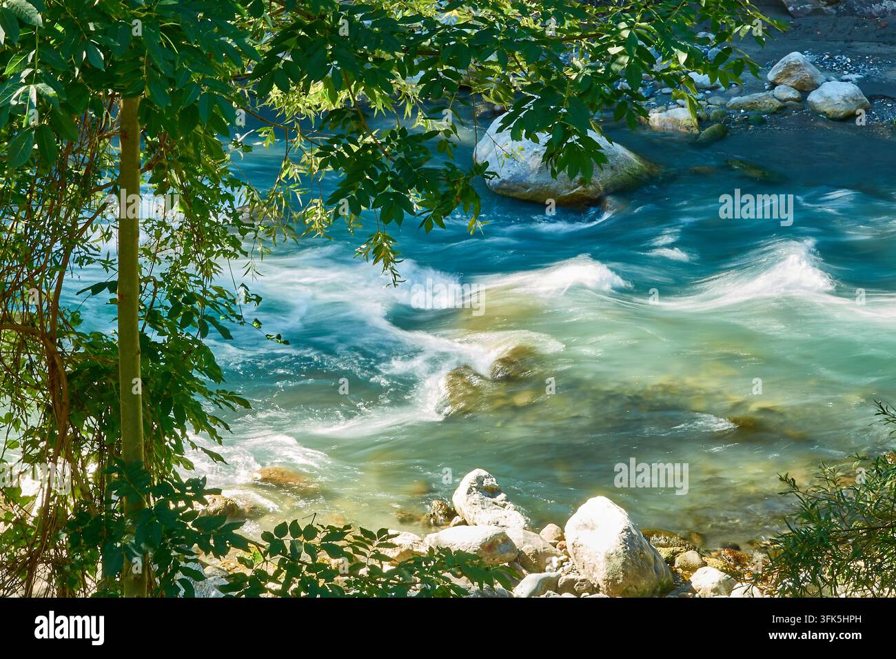Fiume turchese che scorre tra rive rocciose incorniciate da alberi verdi e fogliame illuminato dal sole Foto Stock