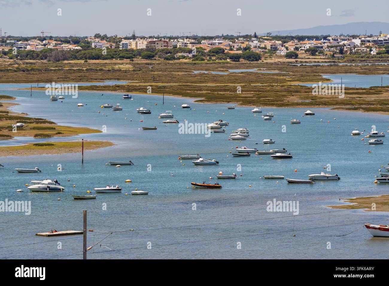 Vista sulle piccole barche ormeggiate nella laguna della Ria Formosa con lo skyline della città di Faro sullo sfondo, Faro, distretto di Faro, Portogallo. Foto Stock