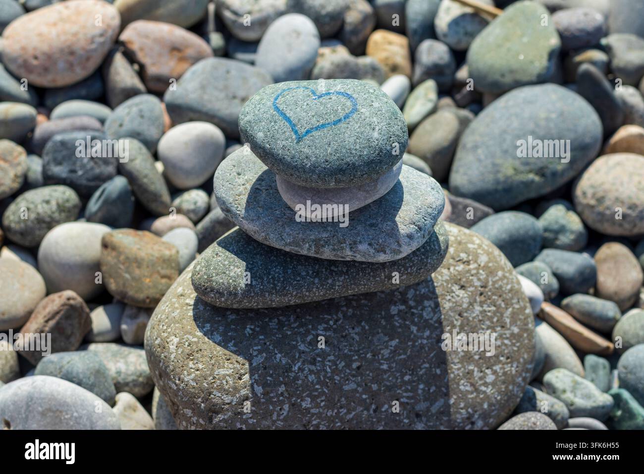 Una pila bilanciata di pietre zen su una spiaggia di ciottoli con un simbolo di cuore blu disegnato a mano. Foto Stock