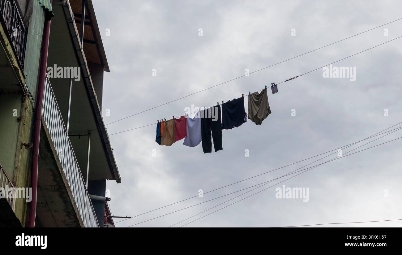Vista ad angolazione bassa di vestiti e biancheria appesa ad asciugare su una corda fuori da un edificio residenziale. Foto Stock