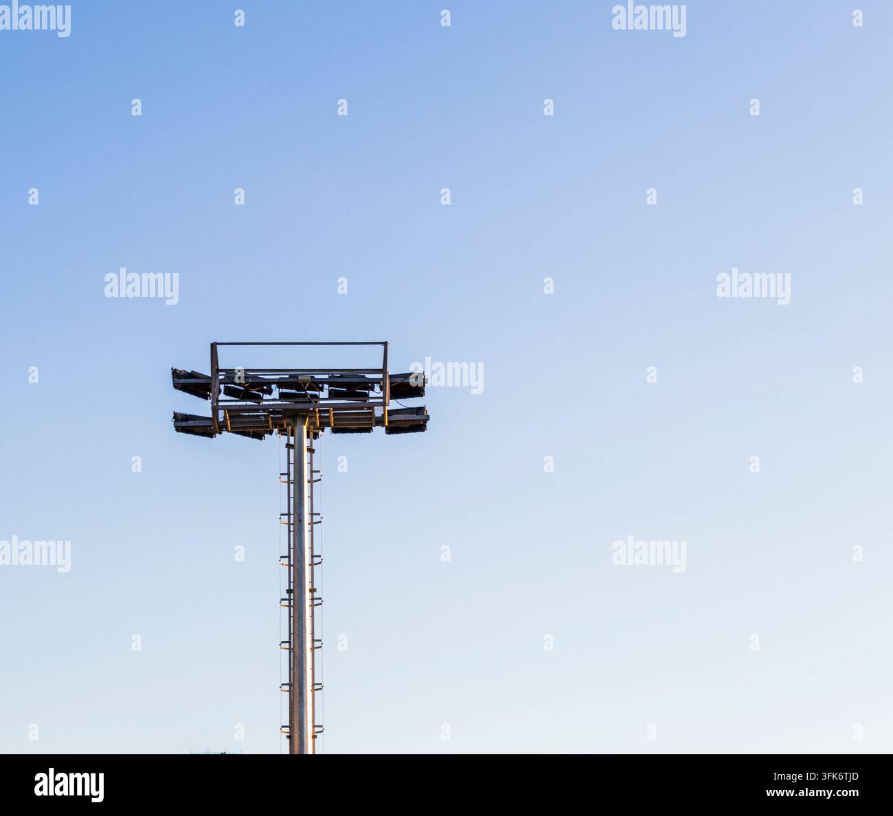 Vista minimalista in basso di un torrione illuminatorio industriale da stadio contro un cielo sereno. Foto Stock