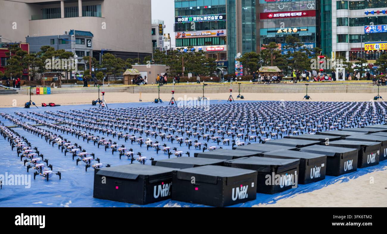 Busan, Corea del Sud - 14 febbraio 2026: Vista di una grande flotta di droni disposti su un telo blu sulla spiaggia in preparazione per uno spettacolo di luci con ambiente urbano Foto Stock