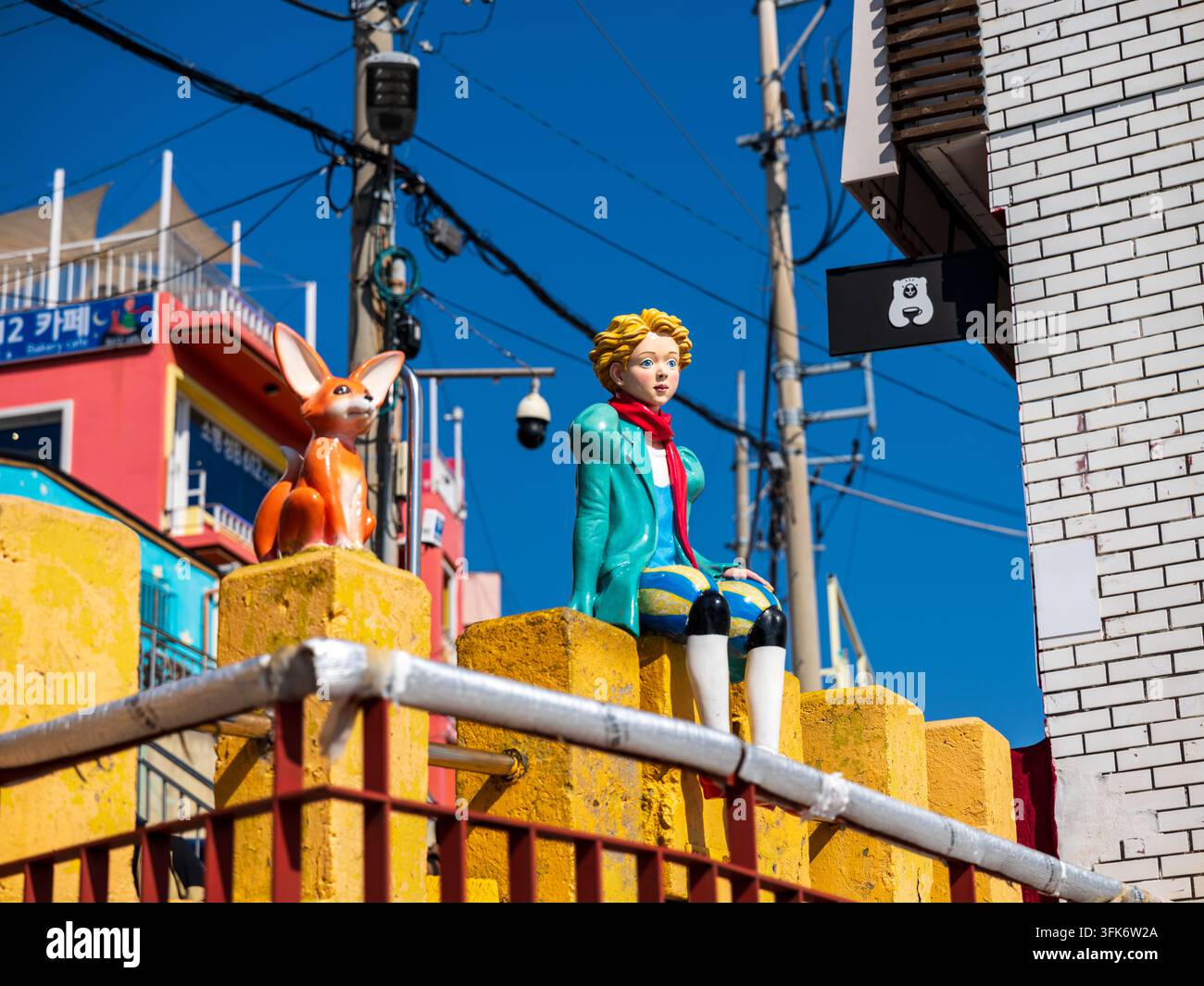 Busan, Corea del Sud - 14 febbraio 2026: Vista delle statue del Piccolo Principe e della volpe su un muro giallo nel villaggio culturale di Gamcheon, con edifici colorati Foto Stock