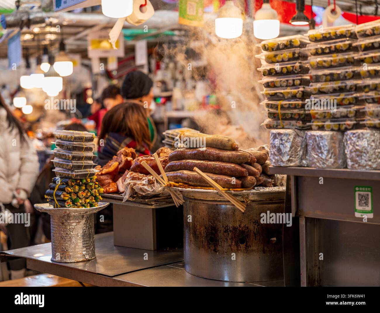 Busan, Corea del Sud - 09 febbraio 2026: Vista di uno stand di street food con salsicce fumanti e pile di kimbap in un mercato affollato. Foto Stock
