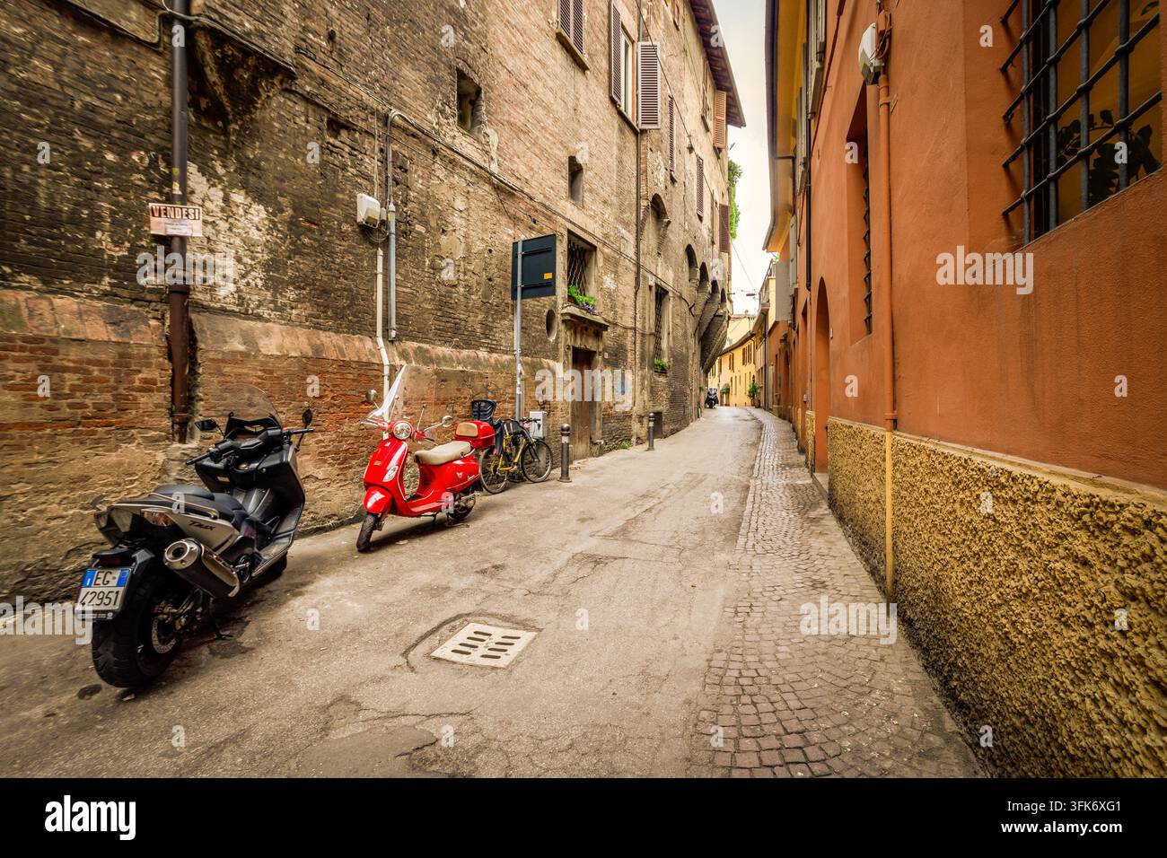 Bologna, Italia - 17 maggio 2018: Vista di una stretta strada acciottolata a Bologna, in Italia, con edifici storici in mattoni, uno scooter rosso parcheggiato e un m Foto Stock