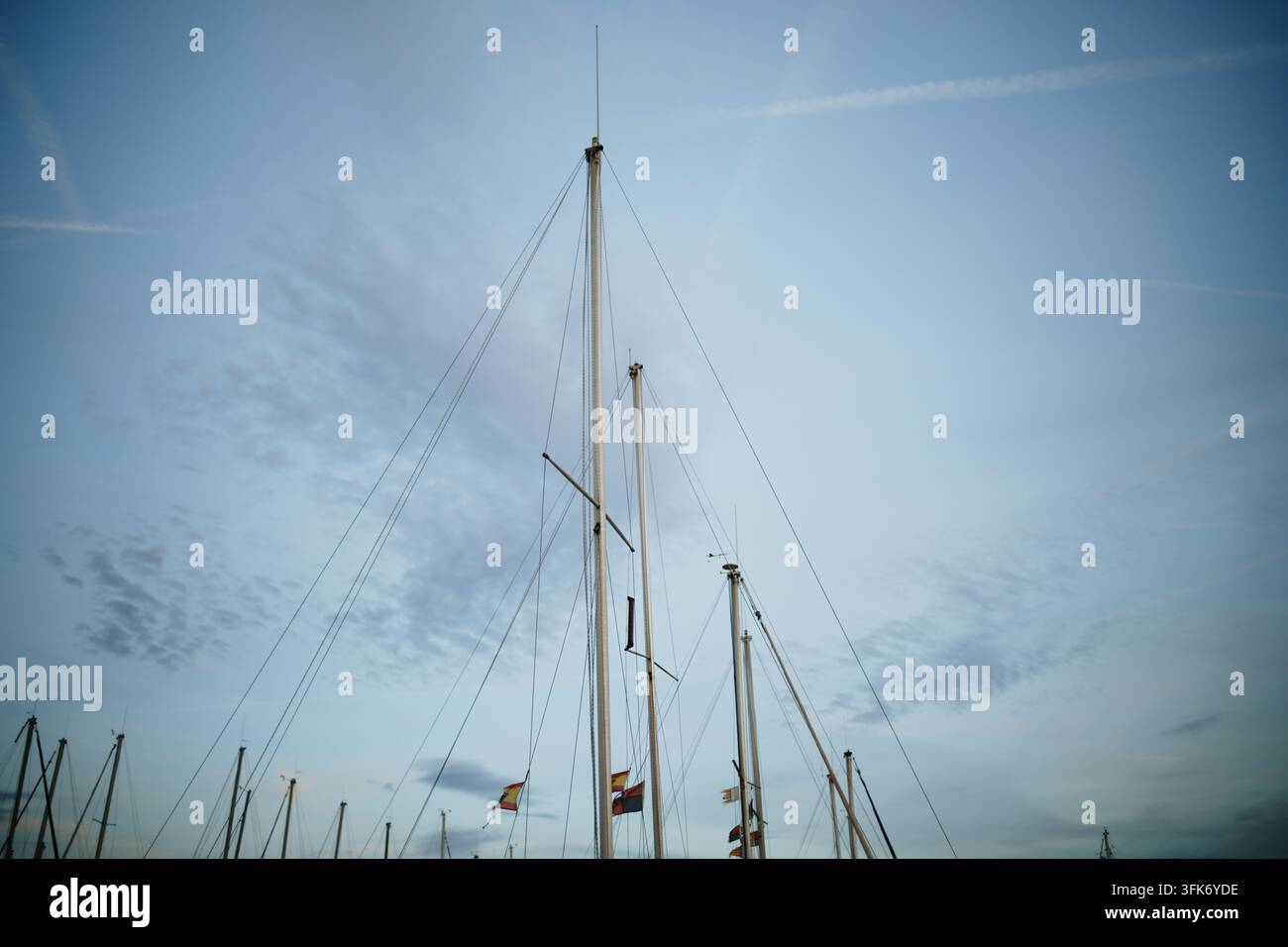 Port de Pollenca, Spagna – 05 gennaio 2025: Vista degli alberi maestri delle barche a vela contro un cielo blu con leggere nuvole nel porto turistico. Foto Stock