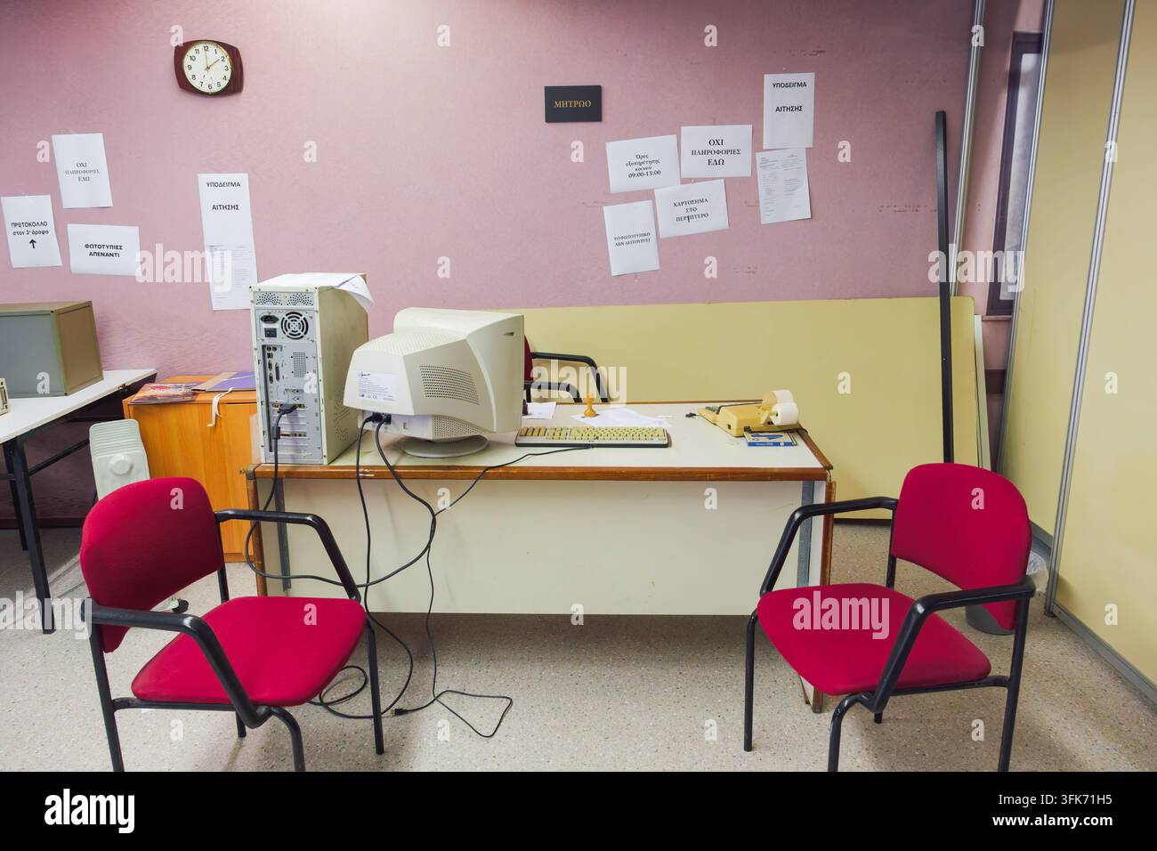 Antico ufficio pubblico con computer vintage, avvisi greci, sedie rosse e scrivanie amministrative. Foto Stock