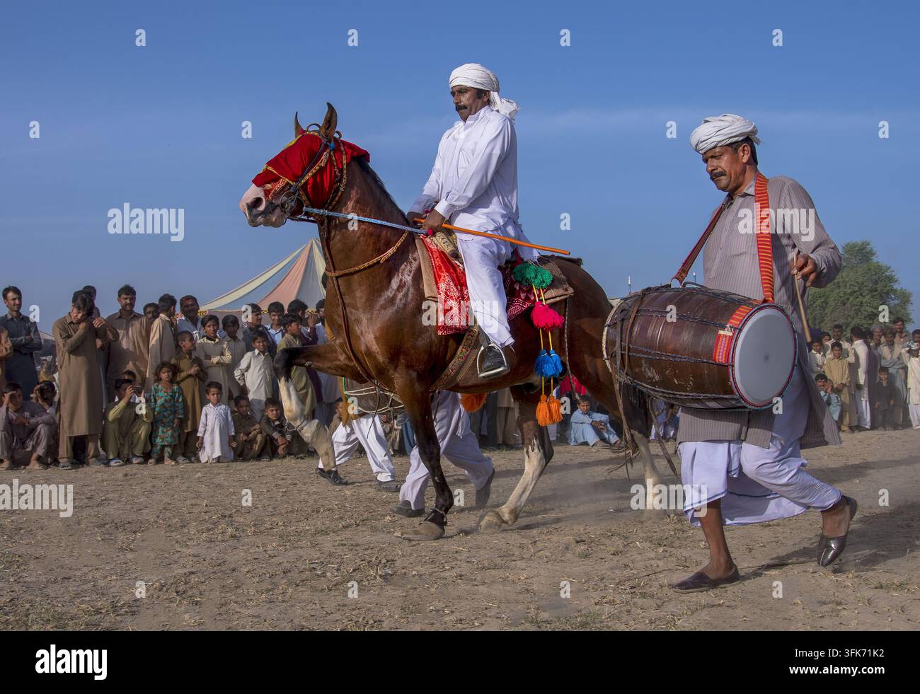Bahawalpur, Punjab, Pakistan – 25 marzo 2025: Vista di una tradizionale esibizione di danza equestre Ghora Nach con un cavaliere su un cavallo decorato e un uomo pla Foto Stock