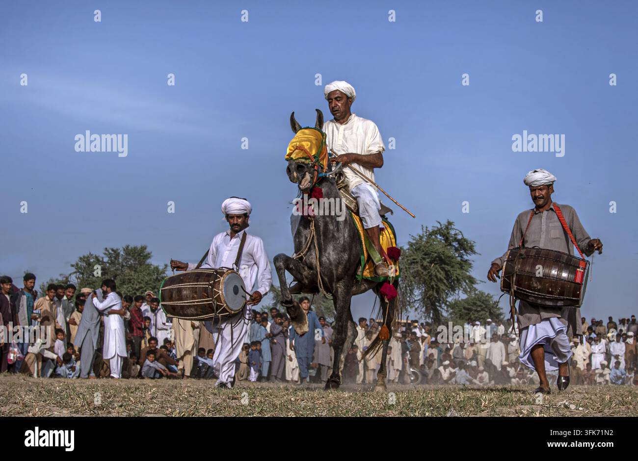 Bahawalpur, Punjab, Pakistan - 25 marzo 2025: Vista di una rappresentazione tradizionale di danza equestre con un cavaliere su un cavallo impennato accompagnato da uomini p Foto Stock