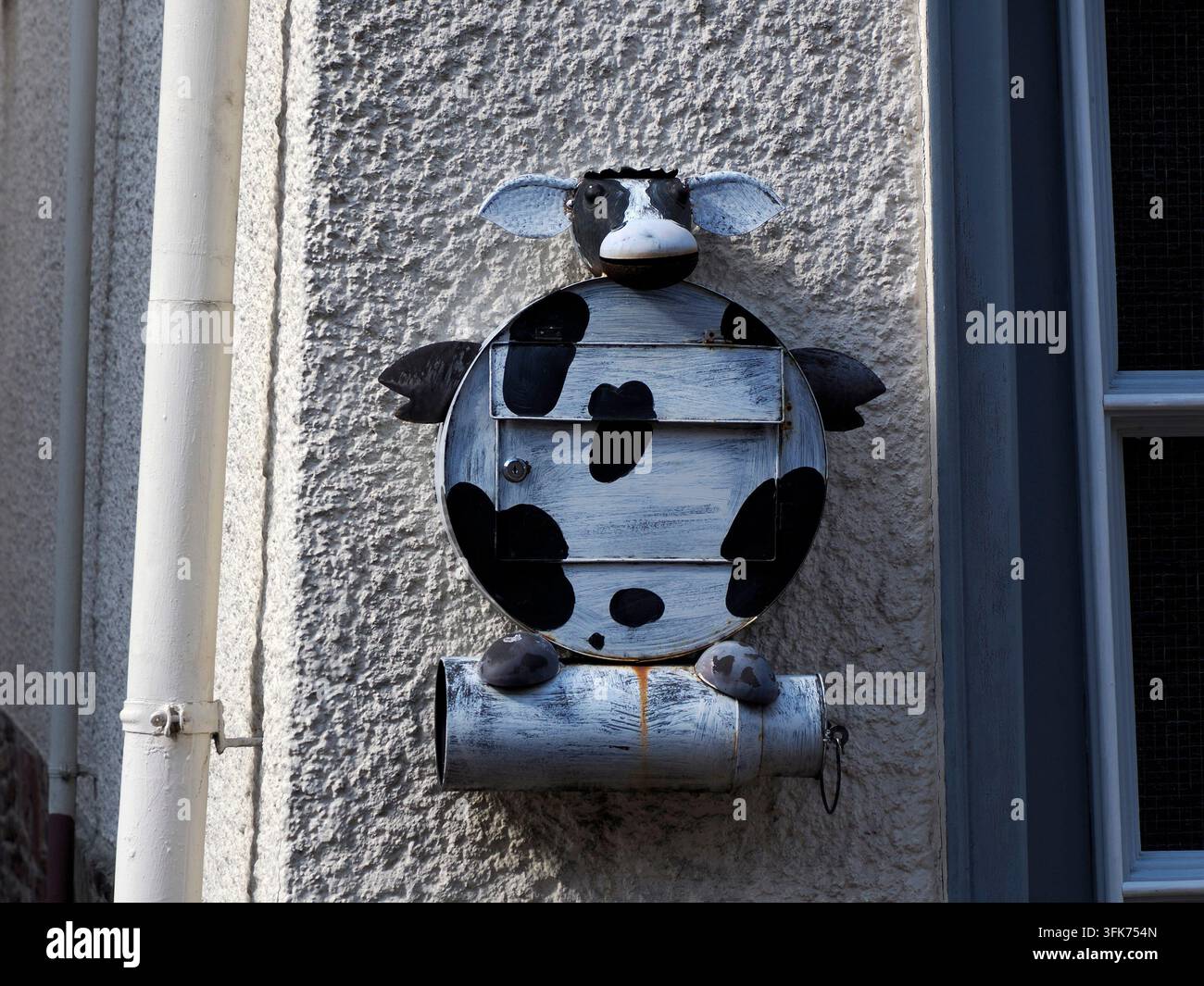 Una cassetta delle poste in metallo creativa fatta a mano progettata come una mucca maculata nera e bianca, montata su un muro in stucco strutturato in Germania. Foto Stock