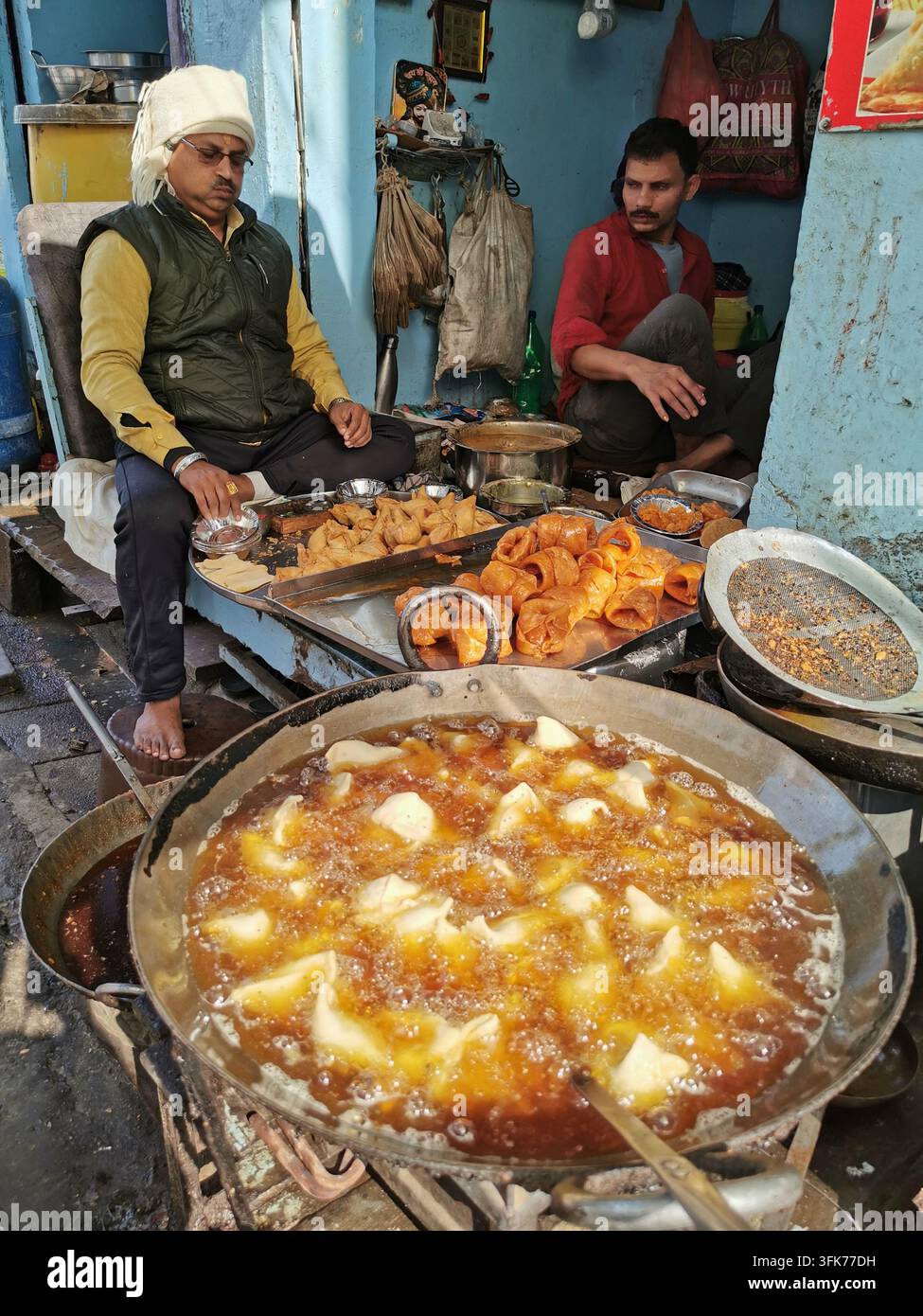VARANASI, INDIA - 23 GENNAIO 2026: I venditori di strada preparano snack fritti e dolci su un banco alimentare a Varanasi. Foto Stock