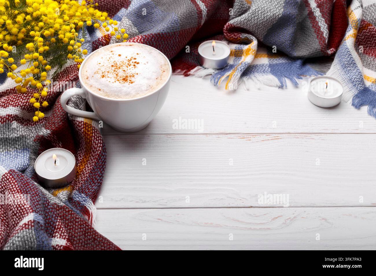 Cappuccino a caffè caldo, coperta, candele, fiori di mimosa su vecchio sfondo in legno. Concetto di relax romantico stagionale, in appartamento Foto Stock