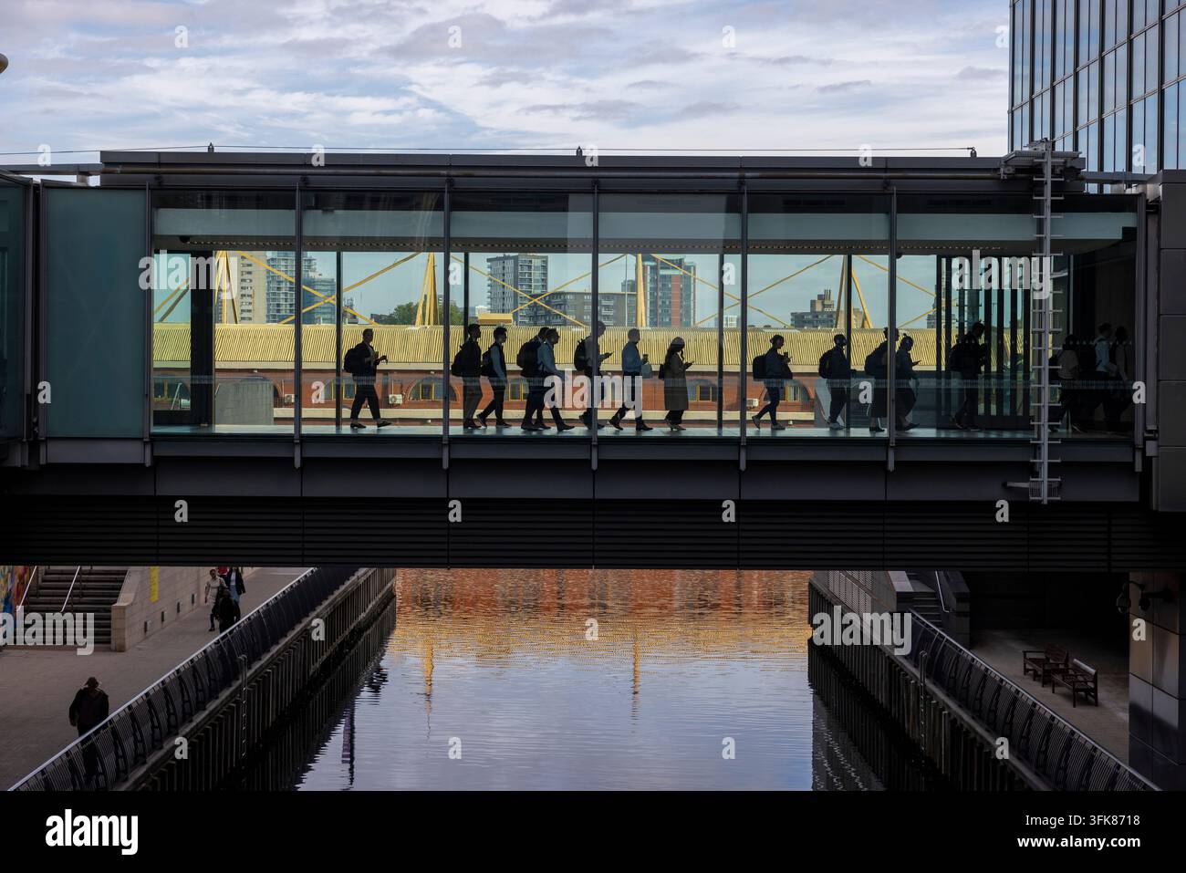Pendolari mattutini che attraversano un ingresso in vetro rialzato verso uffici commerciali nel distretto finanziario dei Docklands di Londra, Canary Wharf, UK Foto Stock