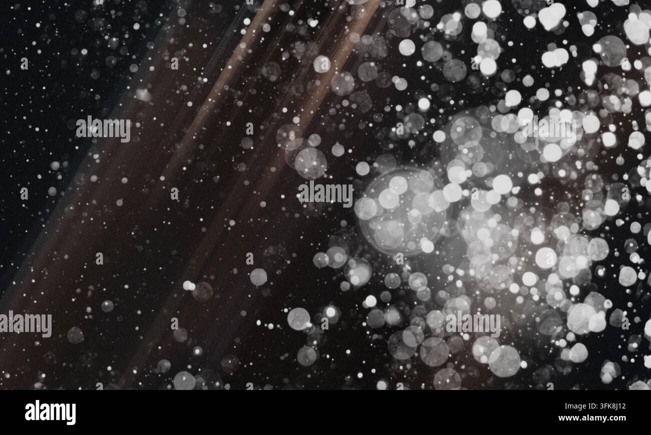 Uno sfondo astratto scuro e suggestivo con strisce di luce diagonali e un campo fitto di cerchi di bokeh bianchi luminosi e sfocati e una grana fine. Foto Stock
