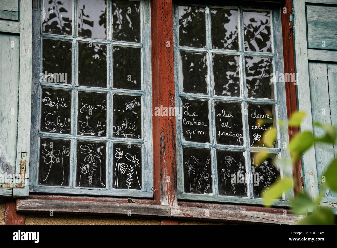 "Buona giornata … La felicità più dolce è quella che condividiamo". Finestra vintage con scritta francese e scarabocchi di fiori con pennarello bianco. Foto Stock