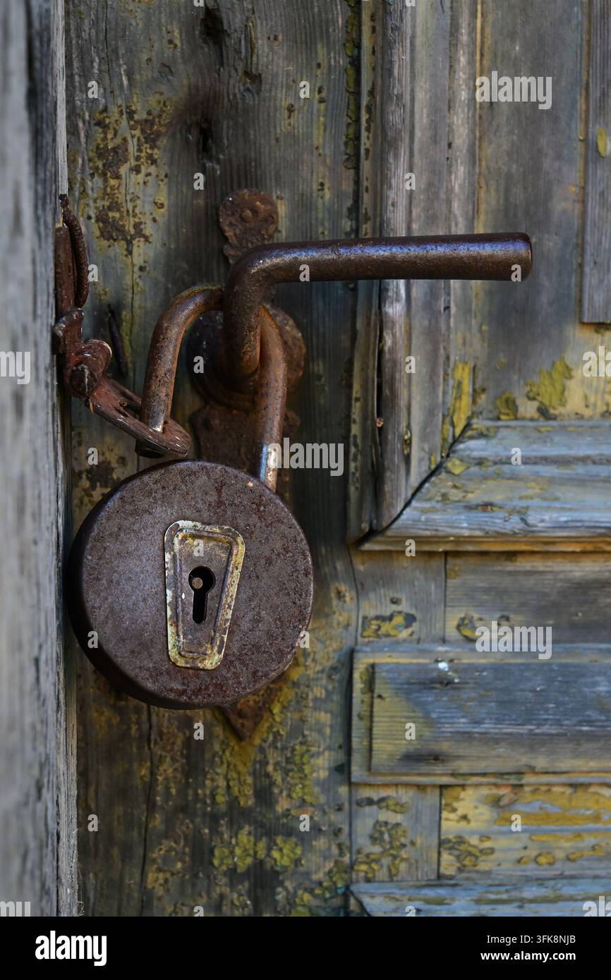 • Lucchetto arrugginito su una vecchia maniglia della porta – simbolo di mistero e di un passato chiuso Foto Stock