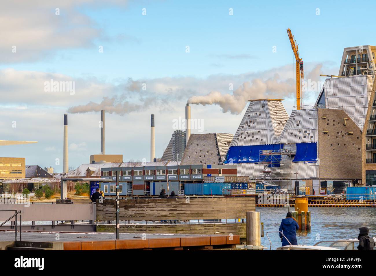 Copenaghena, Danimarca – 02 gennaio 2025: Un paesaggio urbano con camini industriali che emettono vapore affianco a edifici contemporanei in fase di sviluppo Foto Stock