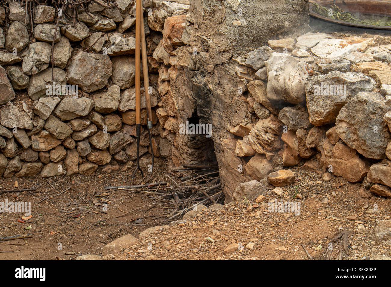 Una traditionalissima bocca di forno in pietra è costruita all'interno di un muro di pietra a secco. È riempita con rametti e rami secchi. Nelle vicinanze, sono pronti strumenti di legno a manico lungo Foto Stock