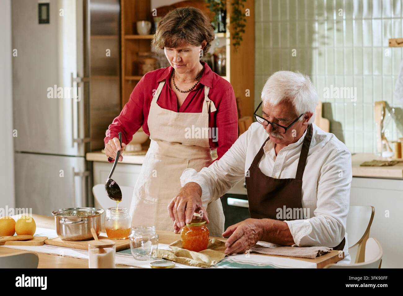 Coppia di anziani che prepara e conserva la marmellata fatta in casa in cucina Foto Stock