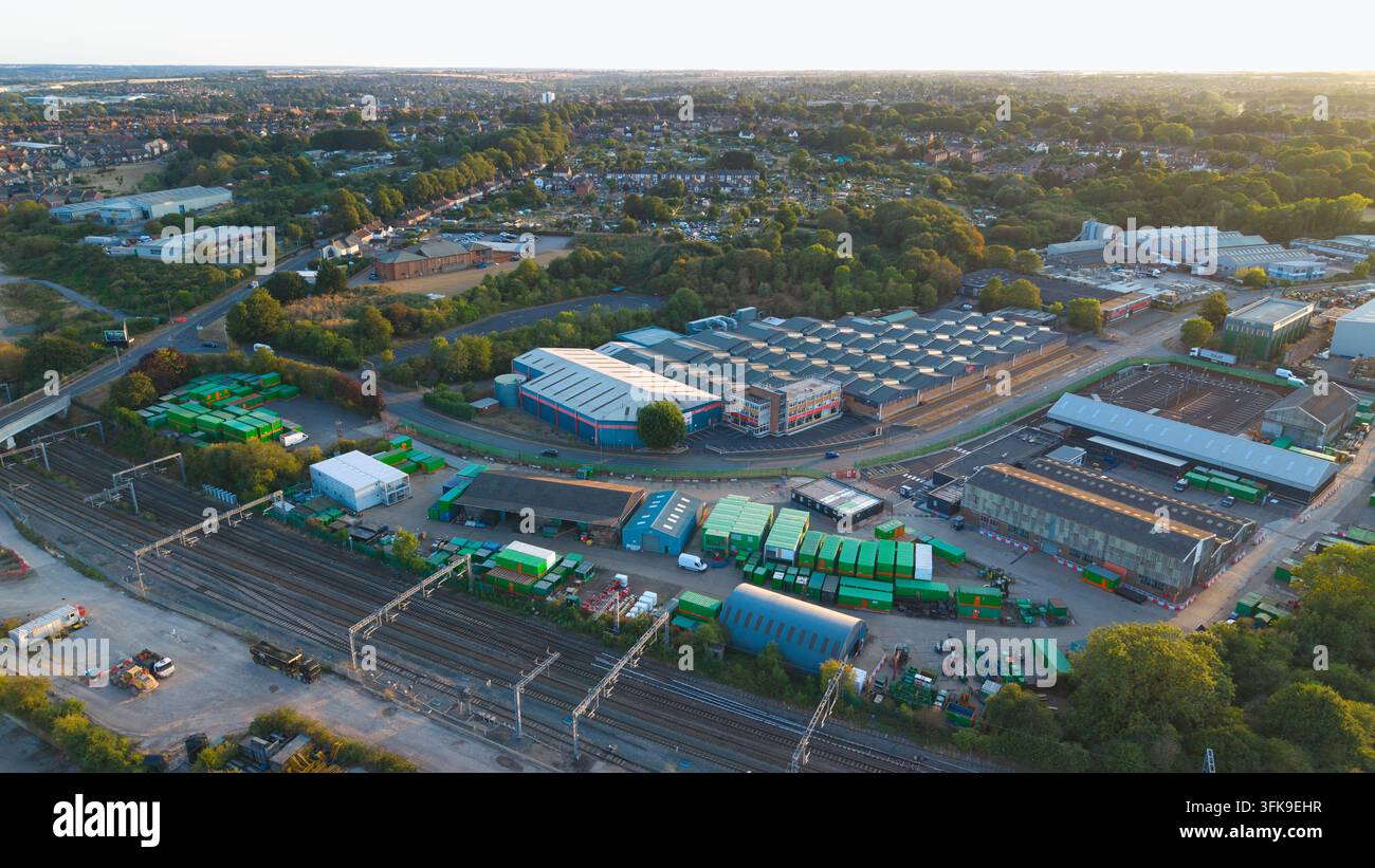 Vista aerea del terminal di carico delle banchine di Wellingborough con container di spedizione, magazzini industriali e binari ferroviari sotto la luce del tramonto a Welli Foto Stock