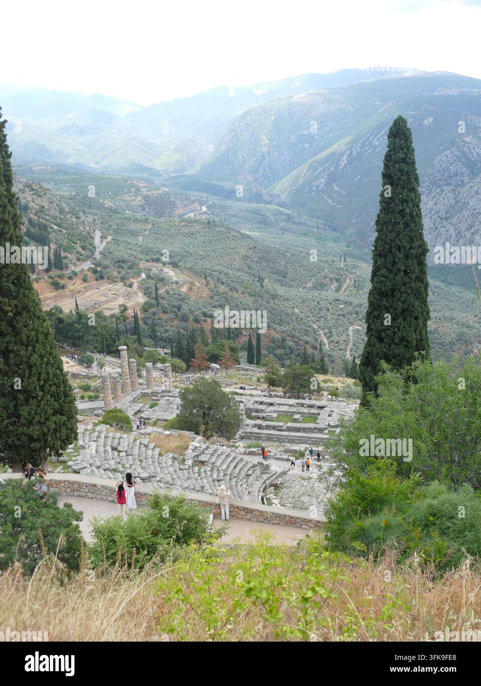 DELFI, GRECIA - 13 MAGGIO 2025 - Turisti che camminano vicino al teatro antico di Delfi godendosi la vista panoramica sulla valle di Pleistos con le montagne sullo sfondo Foto Stock