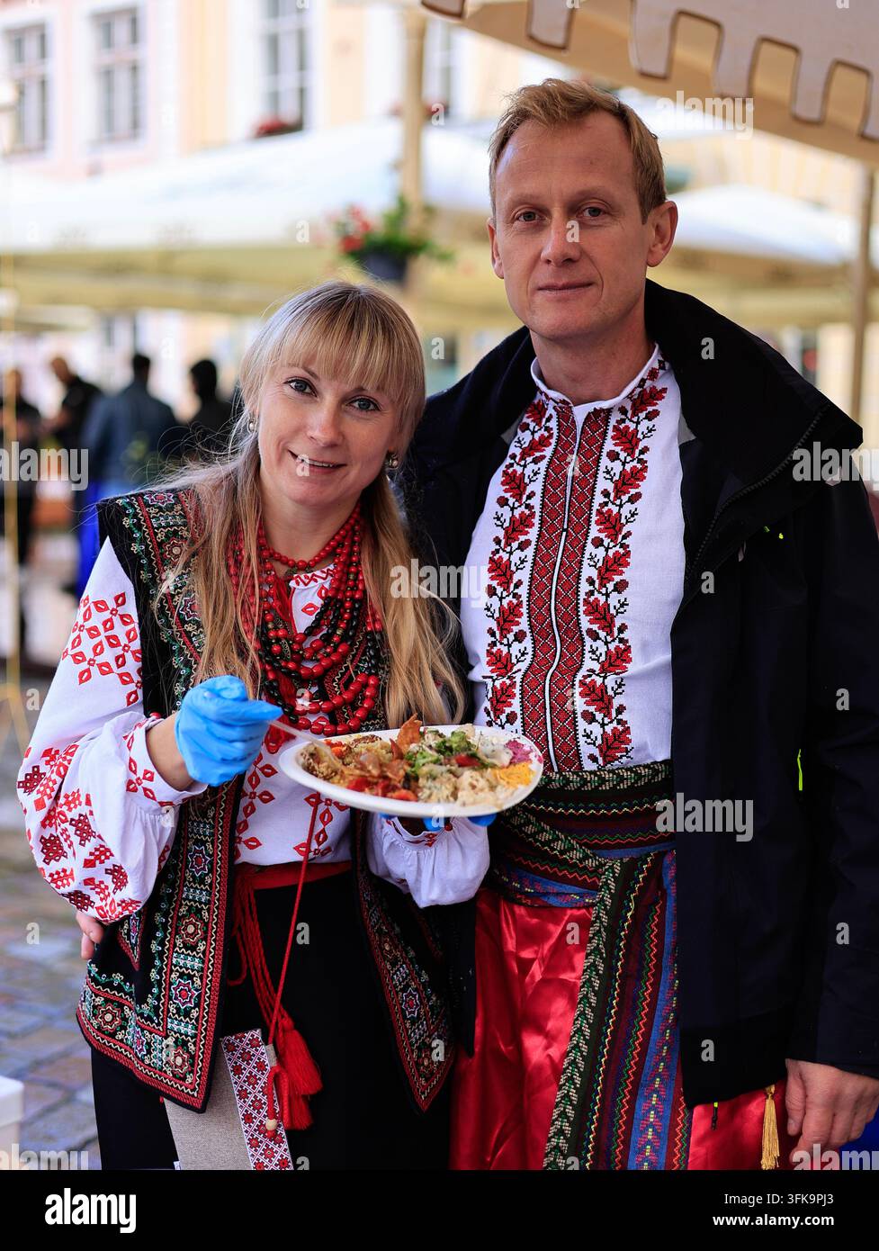 Tallinn, Estonia - 20 settembre 2026: Uomo e donna in costumi tradizionali ucraini tengono un piatto di cibo alla fiera culturale etnica Etnolaat Foto Stock