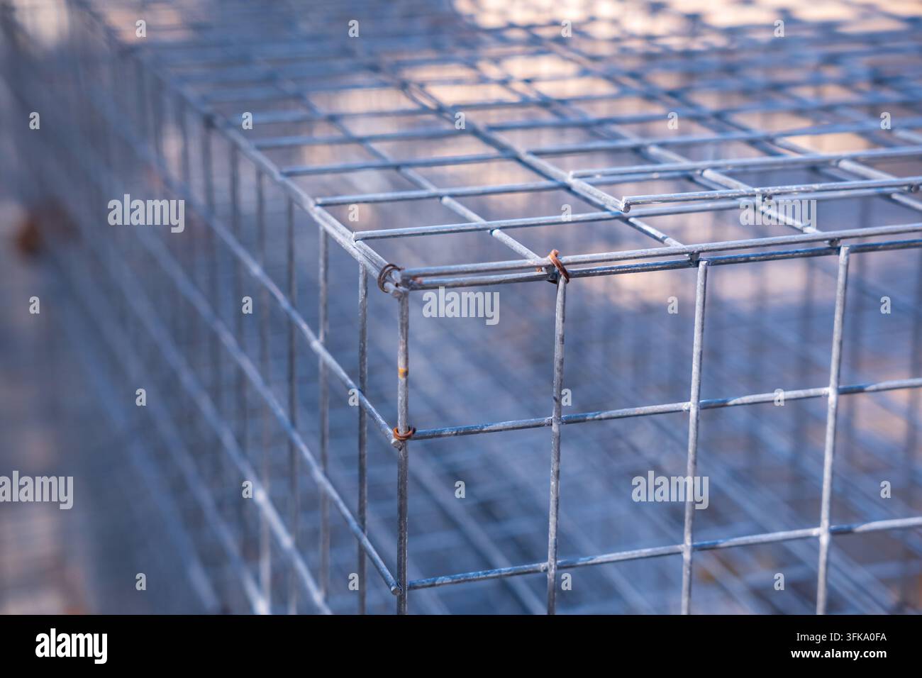 Primo piano di una scatola gabione vuota in maglia metallica zincata, conservata all'aperto in un cantiere edile sotto la luce naturale del sole. Foto Stock