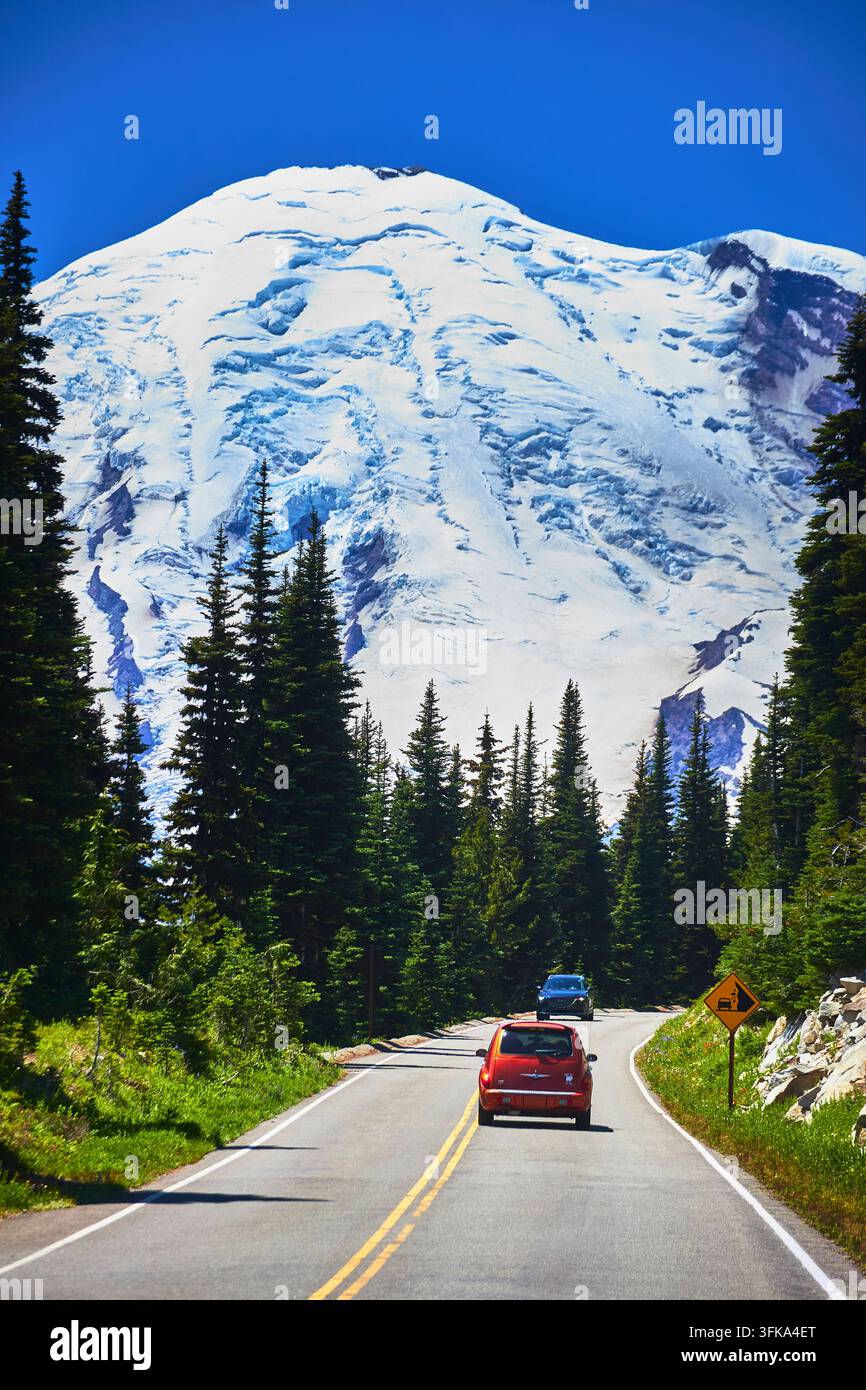 Un'auto si snoda lungo una strada panoramica attraverso la regione di Sunrise del Monte Rainier nello stato di Washington negli Stati Uniti. Picchi innevati imponenti e foreste di conifere lussureggianti Foto Stock
