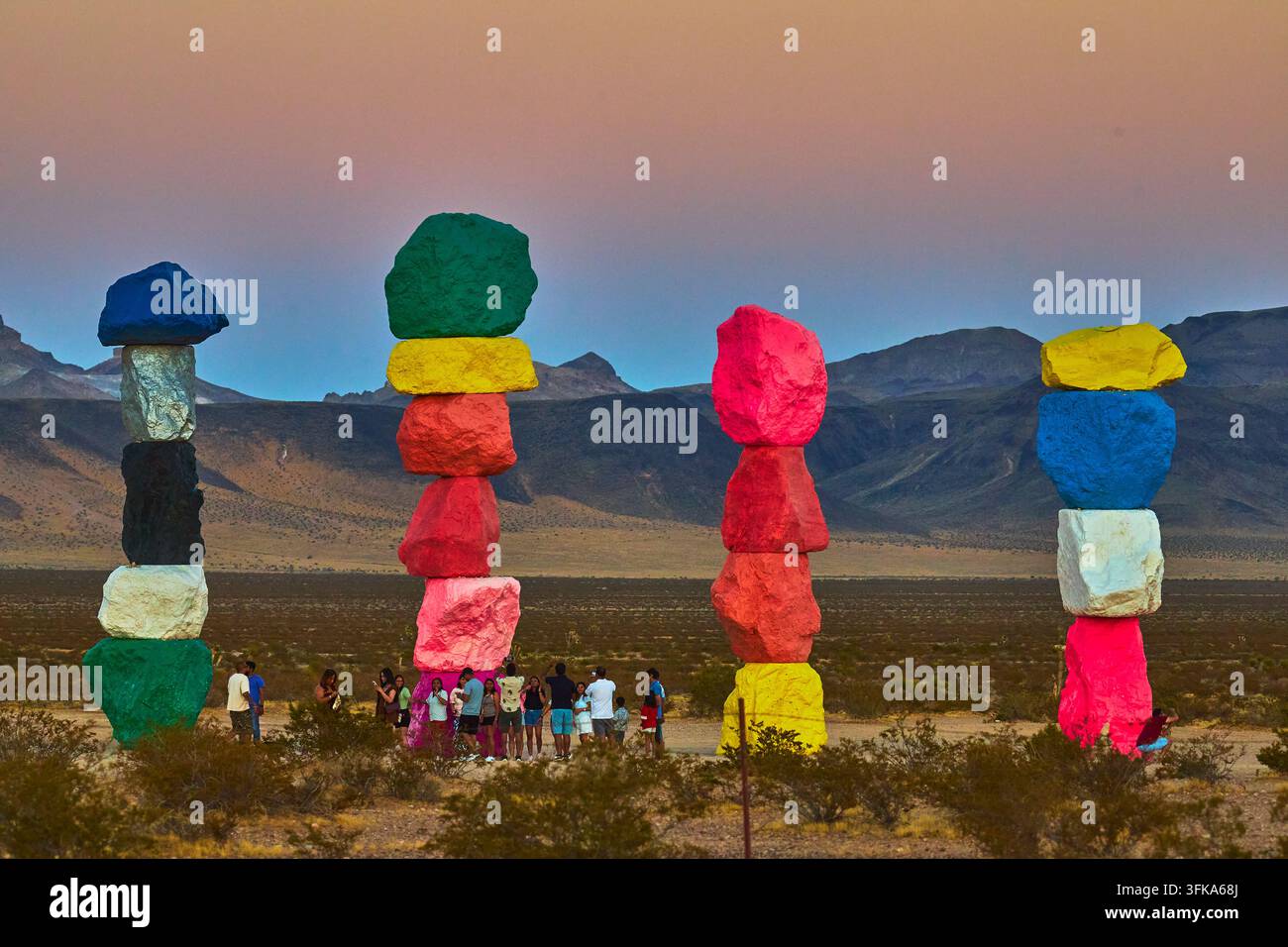 L'installazione artistica The Seven Magic Mountains si erge sopra il deserto del Nevada mentre i visitatori si radunano all'ora dorata. Pietre accatastate vibranti e montagne lontane Foto Stock